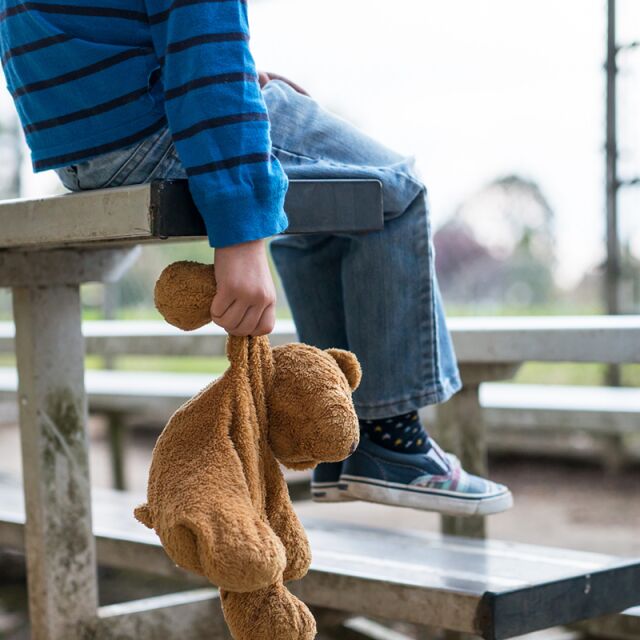 Barnet sitter på en bänk och håller en nalle i handen.