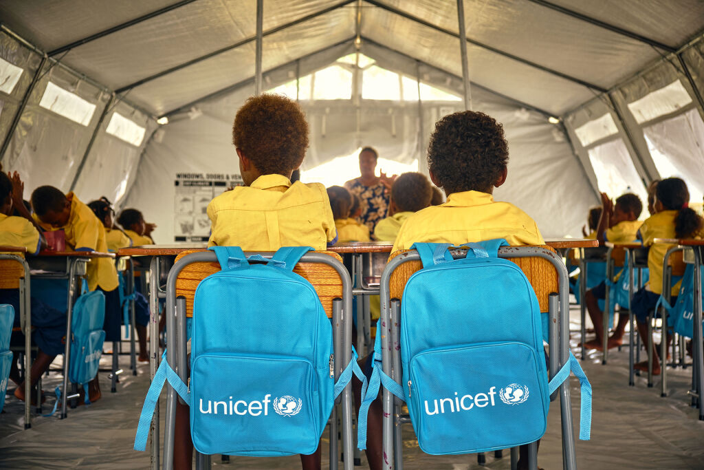 Kaksi koululaista istuu vierekkäin telttakoulussa. Tuolin selkänojilla UNICEF-reput