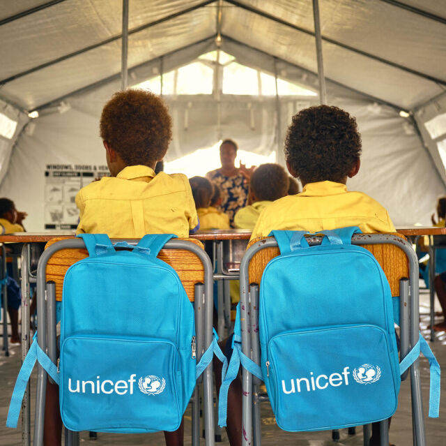 Kaksi takaapäin kuvattua oppilasta. UNICEF-reput roikkuvat tuolin selkänojilla