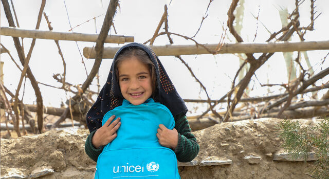 Kuvassa tyttö hymyilee pitäen käsissään UNICEFin koulureppua.