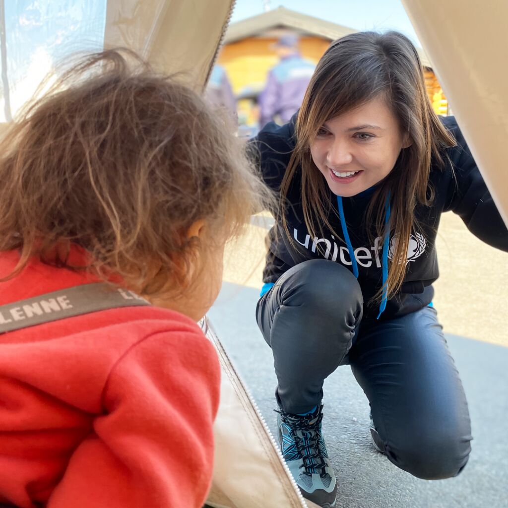 UNICEFin työntekijä keskustlee lapsen kanssa teltan ovensuulla.