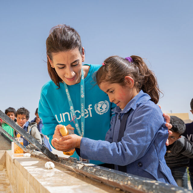 Unicefin työntekijä auttaa tyttöä pesemään kädet.