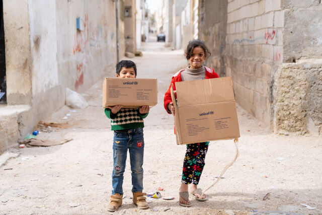 Lapset kantavat UNICEFin avustuslaatikoita iloisin ilmein
