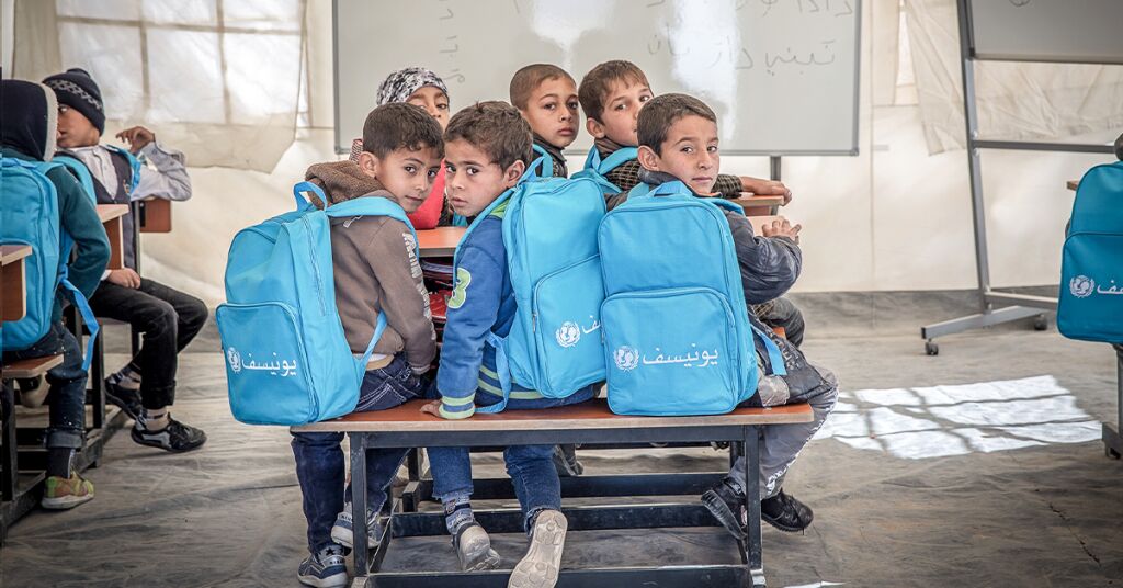 lapsia koulunpenkissä kääntyneenä kameraan UNICEF-reput selässä