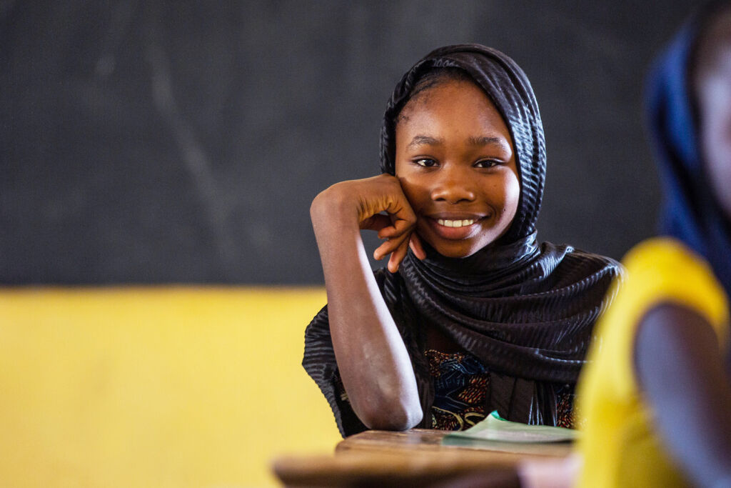 Senegalilainen nuori istuu koulupulpetissa hymyillen